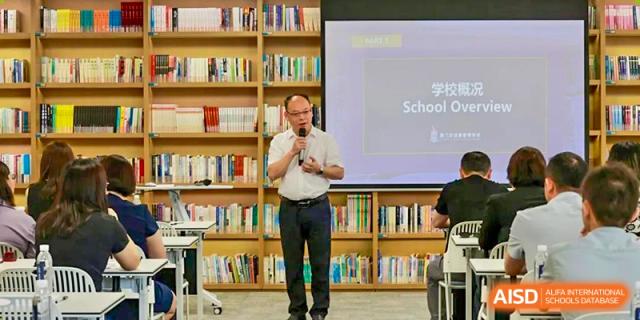 A male teacher at Chiway Bilingual School Xiamen giving a presentation or talk in a library or seminar setting.