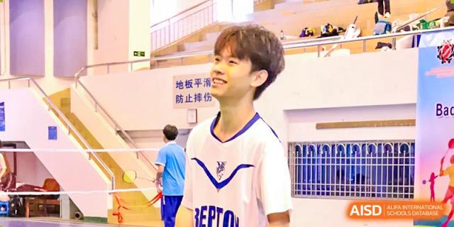 A smiling male student from Chiway Bilingual School Xiamen wearing a white and blue athletic top in an indoor sports facility.