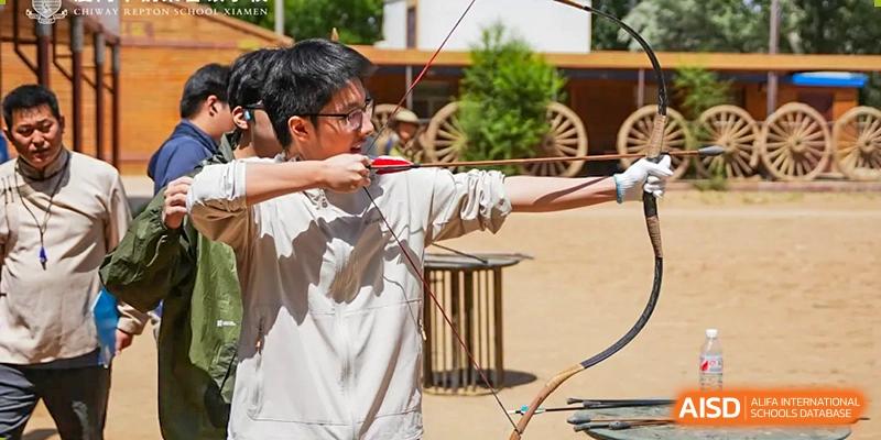 A student from Chiway Bilingual School Xiamen practicing archery outdoors, drawing back the bowstring with focus.