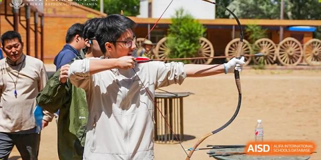 A student from Chiway Bilingual School Xiamen practicing archery outdoors, drawing back the bowstring with focus.