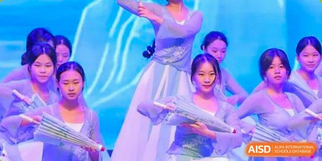 Female students from Chiway Bilingual School Xiamen performing a cultural dance on stage, holding props.