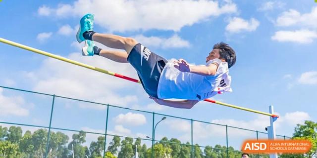 A male student at Chiway Bilingual School Xiamen performing a high jump outdoors against a clear blue sky.