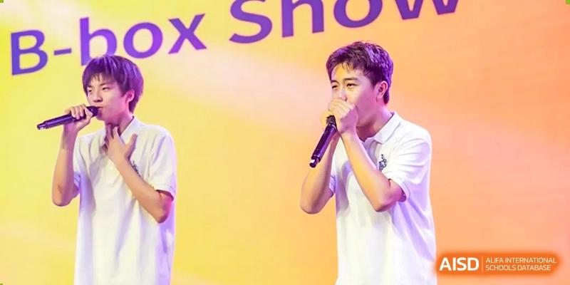 A male student from Chiway Bilingual School Xiamen singing solo into a microphone against a bright yellow and purple background.
