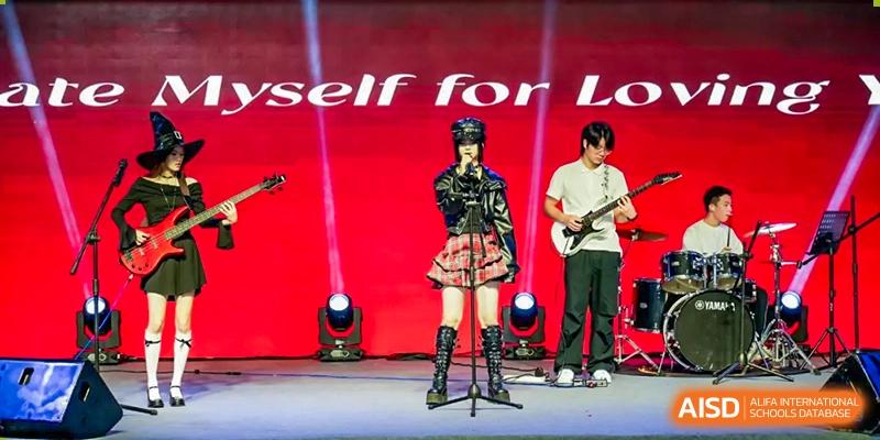 Two students from Chiway Bilingual School Xiamen performing rock music on stage with electric guitars and a microphone stand.