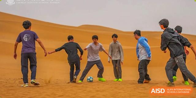 Students from Chiway Bilingual School Xiamen playing soccer on a sandy, desert-like terrain.