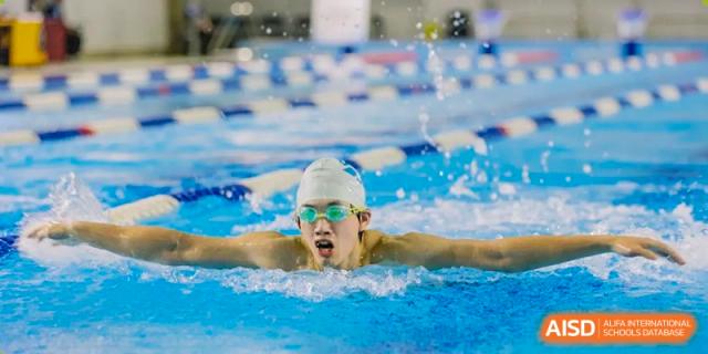 A student from Chiway Bilingual School Xiamen swimming freestyle laps in a competitive indoor pool.