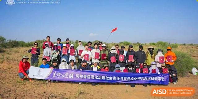A large group of students from Chiway Bilingual School Xiamen posing with certificates outdoors, holding a banner in a dry, sandy field.