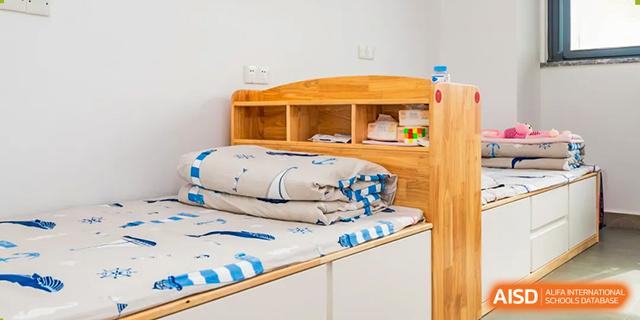 A view of a dormitory bed with wooden shelving and a white mattress cover at Chiway Bilingual School Xiamen.