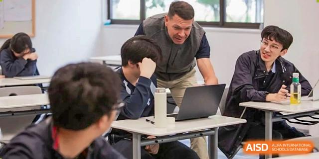 An international teacher from Dipont Huayao Collegiate School Kunshan is helping students who are working on laptops in a classroom.