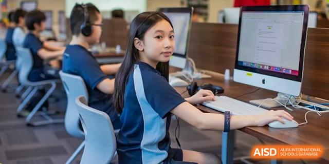 A female student from Dipont Huayao Collegiate School Kunshan is seated at a desk, looking at the camera while using a computer.