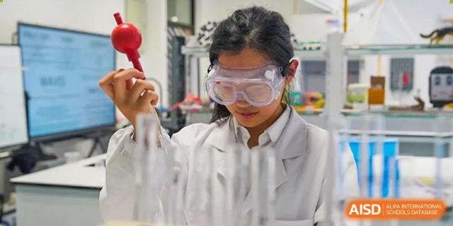 A female student from Dipont Huayao Collegiate School Kunshan, wearing safety goggles and a lab coat, conducts an experiment in a science laboratory.