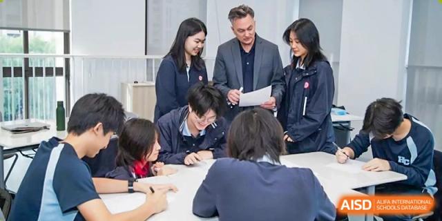 A teacher from Dipont Huayao Collegiate School Kunshan is helping a group of students during a class discussion at a table.