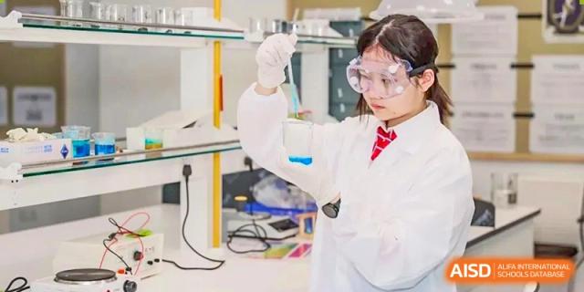 A student from Dipont Huayao Collegiate School Kunshan, wearing safety goggles and a lab coat, holds a test tube during an experiment.