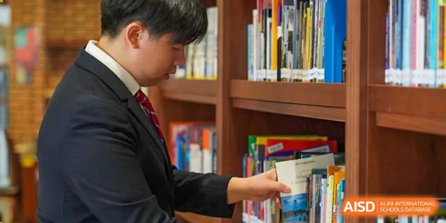 A student from Dipont Huayao Collegiate School Kunshan is looking at a book on a shelf in the library.