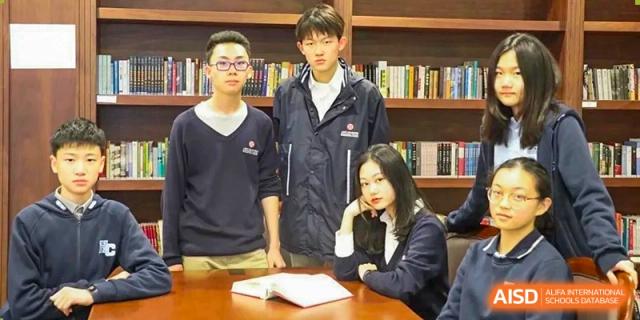 Students from Dipont Huayao Collegiate School Kunshan are gathered around a table in the library, with an open book.