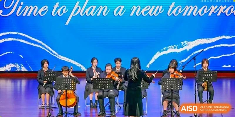 A student orchestra from Dipont Huayao Collegiate School Kunshan performs on a stage during an event.