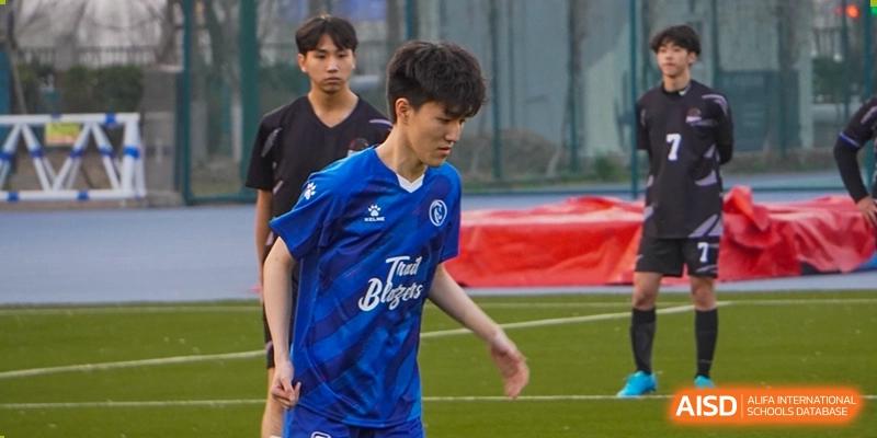 A student from Dipont Huayao Collegiate School Kunshan in a blue jersey is playing football on a green field.