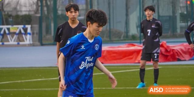 A student from Dipont Huayao Collegiate School Kunshan in a blue jersey is playing football on a green field.