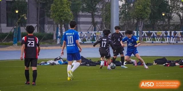 Students from Dipont Huayao Collegiate School Kunshan are playing football on a green field.