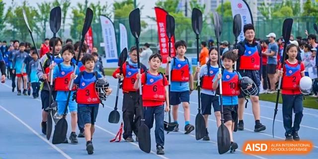 Students from Dipont Huayao Collegiate School Kunshan are walking while holding paddles and wearing life vests.
