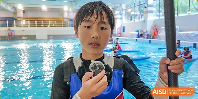 A student from Dipont Huayao Collegiate School Kunshan, wearing a life vest, holds a microphone and looks at the camera.