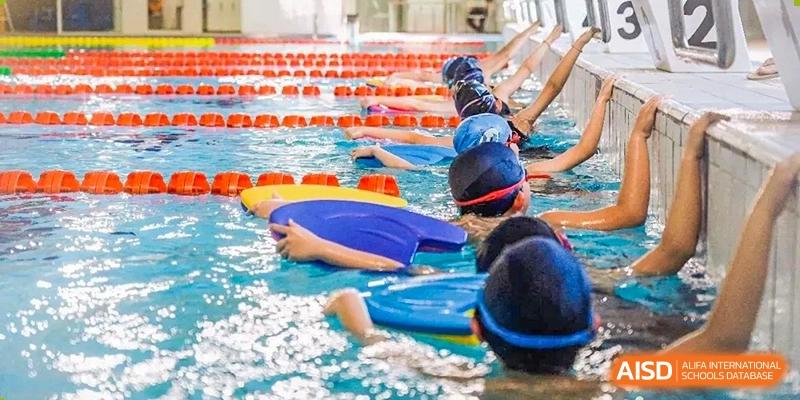 Students from Dipont Huayao Collegiate School Kunshan are participating in a swimming or water sports activity in a pool, with some using floating boards.