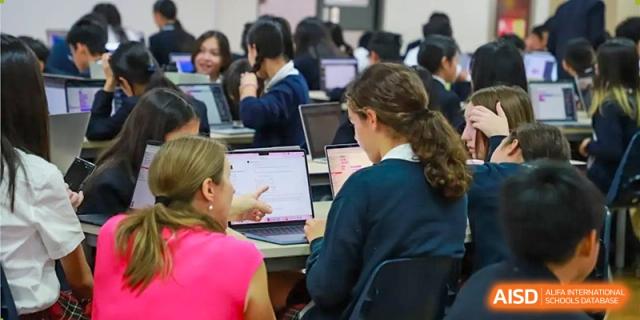 A teacher from Dulwich College Beijing is helping a student with a laptop in a classroom.