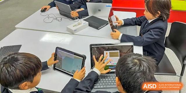 Students from Dulwich College Beijing are collaborating on a project using laptops and tablets at a table.