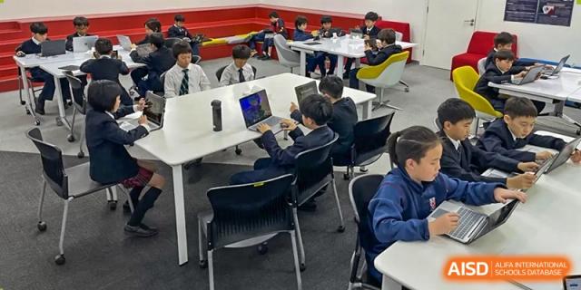 Students from Dulwich College Beijing are sitting at desks using laptops in a modern classroom setting.