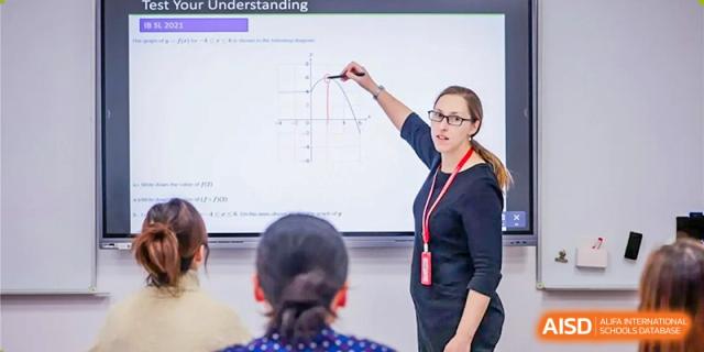 A teacher from Dulwich College Beijing is pointing to a graph on an interactive whiteboard during a lesson.
