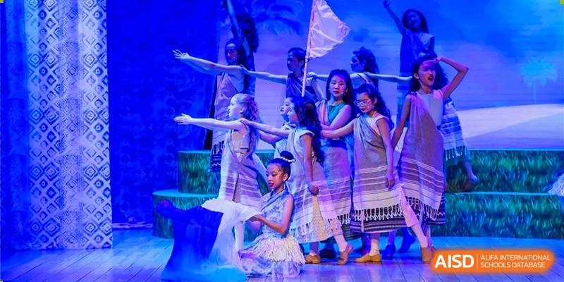 Dulwich College Beijing A group of students in traditional attire performs a dance on a stage with a blue background.