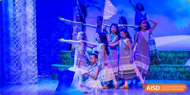Dulwich College Beijing A group of students in traditional attire performs a dance on a stage with a blue background.