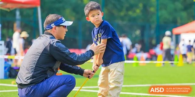 Dulwich College Beijing A young boy receives golf instruction from an adult on a grassy field.