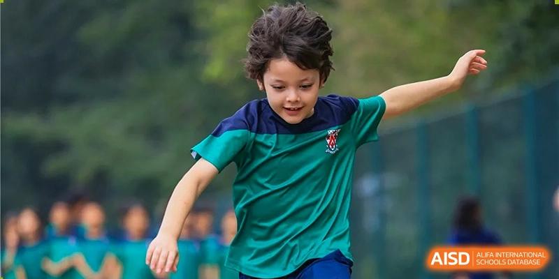 Dulwich College Beijing A young boy in a green and blue shirt is running outdoors.