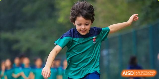 Dulwich College Beijing A young boy in a green and blue shirt is running outdoors.