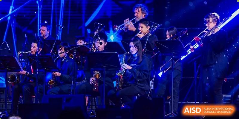 Dulwich College Beijing A jazz band of students plays instruments on a stage with blue and purple lighting.