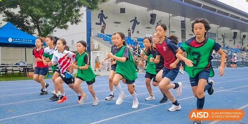 Students at Dulwich College Beijing in green uniforms run a race on a blue track during a sports day.