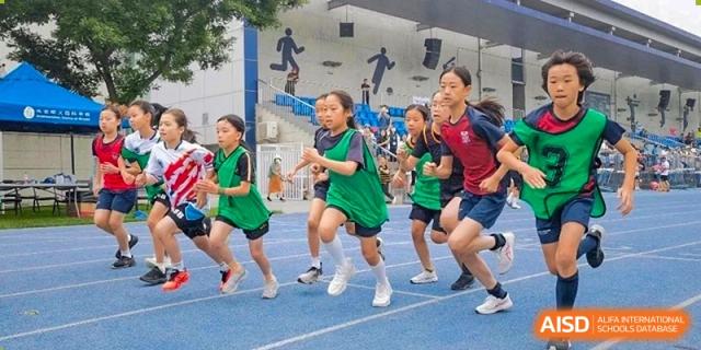 Students at Dulwich College Beijing in green uniforms run a race on a blue track during a sports day.