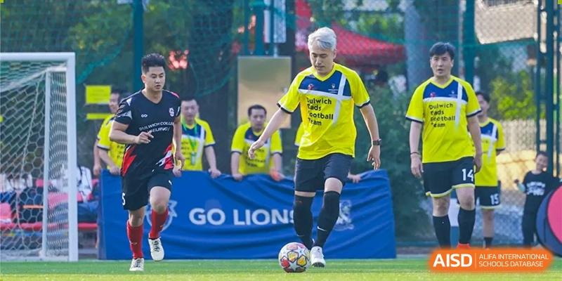 A man wearing a yellow and blue soccer jersey from Dulwich College Beijing is playing soccer.