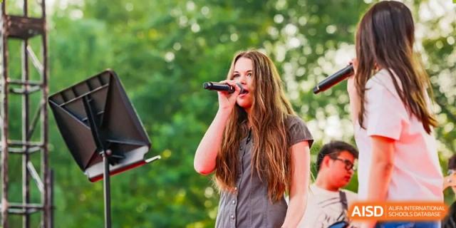A young woman is singing into a microphone at an event for Dulwich College Beijing.