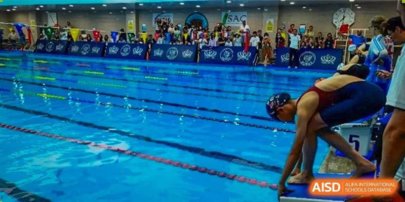 A swimmer is in a swimming pool with spectators from Dulwich College Beijing in the background.