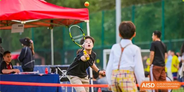 A boy is playing tennis with a tennis racket at a Dulwich College Beijing event.