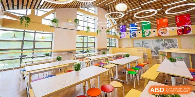 The empty school cafeteria at Dulwich College Beijing, with wooden tables and colorful stools.