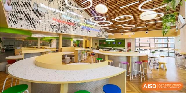 A close-up view of the empty school cafeteria at Dulwich College Beijing, featuring a large circular seating area and modern lighting.