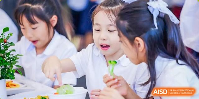 A young girl at Dulwich College Beijing smiling while enjoying a snack with other children.