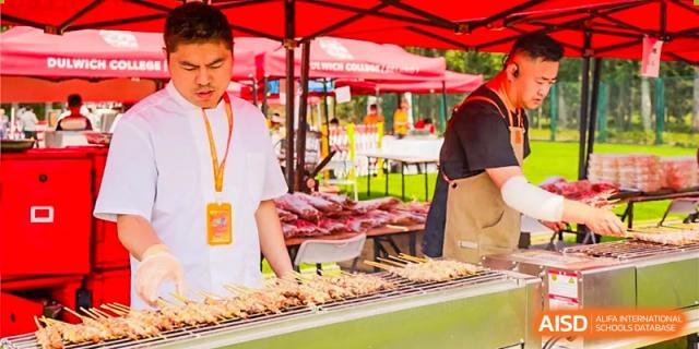 A chef grills food skewers under a red tent at a food stall during a school event at Dulwich College Beijing.