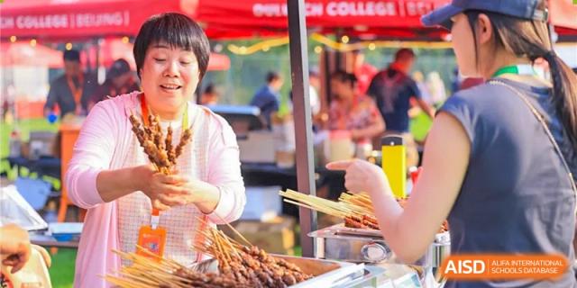 A woman laughs while buying food skewers from a vendor at a festival at Dulwich College Beijing.