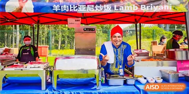 A man in a red turban smiles at a food stall during an outdoor event at Dulwich College Beijing.