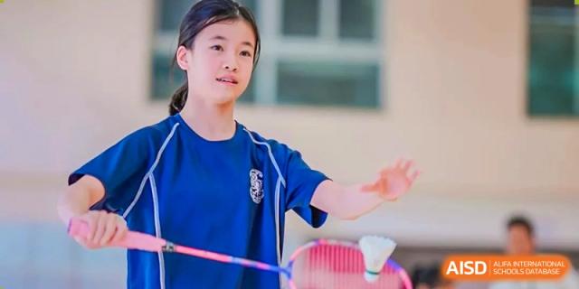 A female student from Harrow International School Shanghai preparing to hit a shuttlecock during a badminton match.