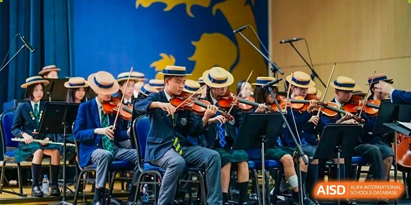 Students from Harrow International School Shanghai playing violins on a stage.